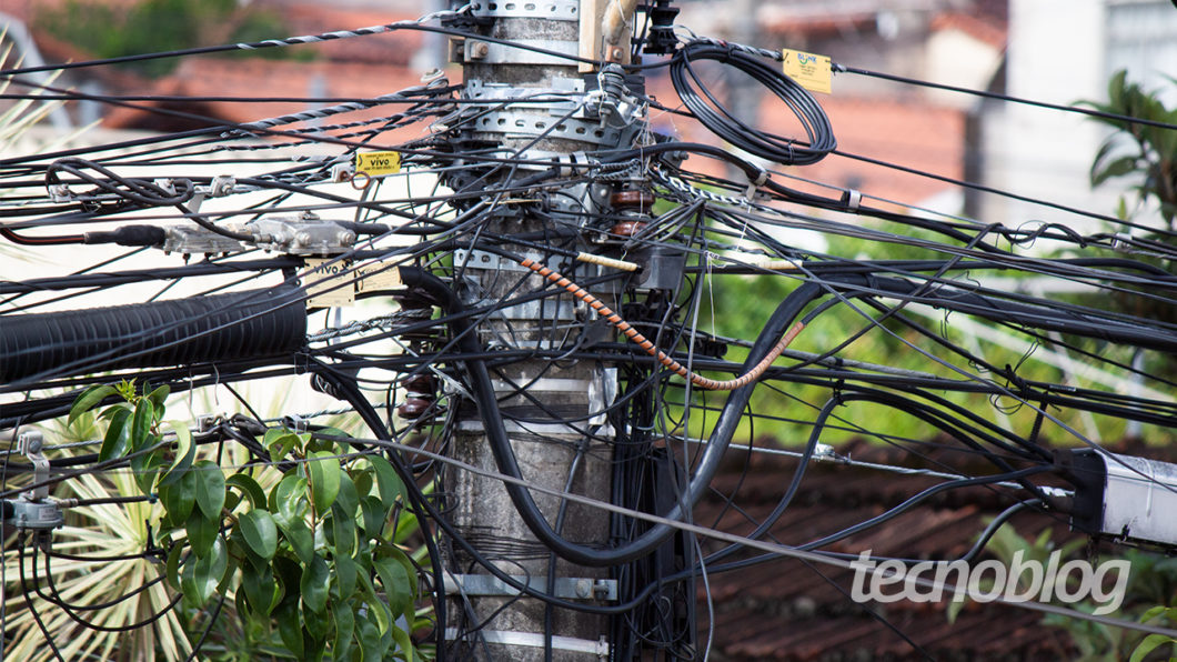 Um monte de cabos de telecomunicações pendurados num poste de energia